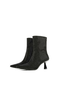 Čierne členkové topánky s priliehavým strihom, ozdobené kovovými detailmi a špicatou špičkou. Na stiletto podpätku.