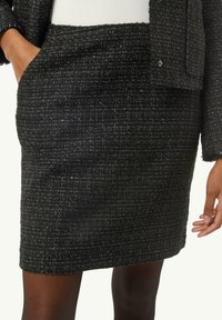 Czarna spódnica z tweedu o teksturowym wykończeniu, o długości powyżej kolan, z kieszeniami. Srebrne nici dodają subtelnego kontrastu do projektu.