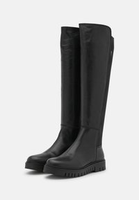 Botas de cuero negro hasta la rodilla con una textura suave, suela de goma y acentos acanalados en la parte superior. Diseño elegante adecuado para varios conjuntos.
