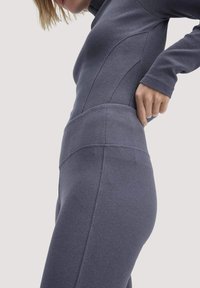 Donkergrijze geribbelde stof activewear set met een aansluitend ontwerp, hoge tailleband en lange mouwen. Naadtoespraken zichtbaar langs de torso.