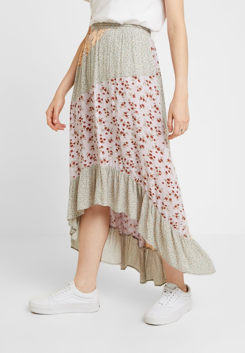 Jupe maxi fleurie avec un ourlet asymétrique, des volants superposés et un mélange de motifs pêche, vert et blanc. Accordée avec des baskets blanches.