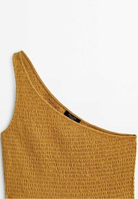 Haut moutarde jaune texturé à une épaule avec un détail en tissu smocké et un décolleté large. Étiquette visible près du col sur le côté.