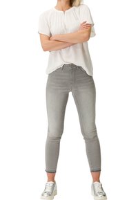 Světlé šedé skinny džíny s středním pasem a jemným vyblednutím, doplněné volnou krémovou blůzou a stříbrnými teniskami.