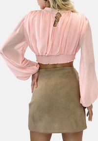 Rosa plissierte Bluse mit Ballonärmeln, tailliertem Schnitt und einem Schlüssellochdetail auf der Rückseite, kombiniert mit einem tanfarbenen Wildleder-Minirock.