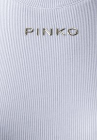 Tessuto bianco a coste con logo "PINKO" in rilievo dorato al centro. La texture è liscia con strisce verticali.