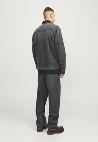 Giacca di jeans nera con vestibilità rilassata, abbinata a pantaloni grigi scuri a taglio largo. Entrambi presentano una texture liscia e un design minimalista.