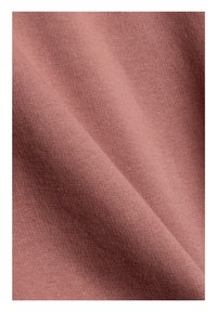 Tissu doux et plié de couleur rose poudrée atténuée avec une texture lisse et étroitement tissée visible en gros plan.