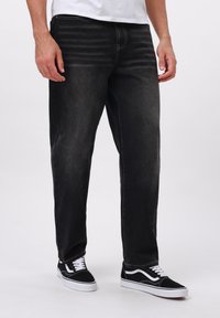 Vaqueros de mezclilla negra con corte recto, con un ligero desgaste y costuras naranjas. Llevados con zapatillas negras y blancas.