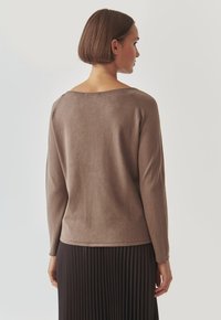 Brauner langärmliger Pullover mit weitem Ausschnitt, weichem Material und geripptem Saum, kombiniert mit einem schwarzen plissierten Rock. Rückansicht.