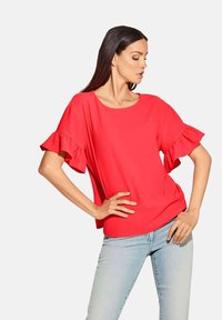 Rotes kurzärmliges Top mit Rüschensäumen, Rundhalsausschnitt und lockerer Passform. Kombiniert mit hellblauen Jeans. Glatte Textur und lebendige Farbe.