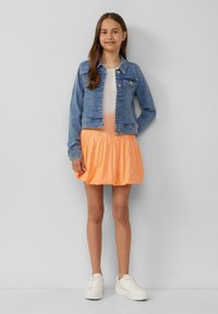 Jeansjacke in hellblauer Wasche, orangefarbener, ausgestellter Rock und weiße Sneakers. Einfaches Design ohne Muster oder Akzente.