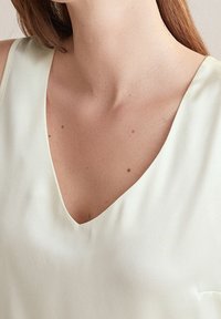 Top V-inserto di colore crema chiaro realizzato in tessuto morbido, caratterizzato da una vestibilità rilassata e una leggera lucentezza, con un collo pulito e una morbida caduta.