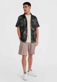 Korte mouwen zwarte shirt met een wit tropisch bladerenpatroon, beige t-shirt eronder, lichtroze cargoshorts en witte sneakers.
