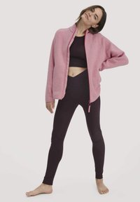 Giacca in pile rosa con chiusura a zip, scollo tondo e zip a contrasto. Top nero corto e leggings neri a vita alta.