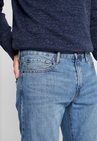 Ljusblå denimjeans har en klassisk design med fem fickor, en knapp- och dragkedjestängning samt diskreta sömnadsdetaljer vid sömmarna.