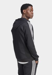 Μαύρη hoodie με εφαρμοστό σχέδιο, που διαθέτει λευκές ρίγες κατά μήκος και των δύο μανικιών και ribbed μανσέτες. Μαλακή υφή, ελάχιστη λεπτομέρεια.