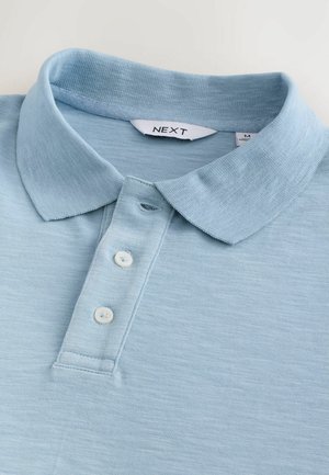 Light blue polo shirt made of woven fabric. Features a button placket with three white buttons and a soft, ribbed collar.