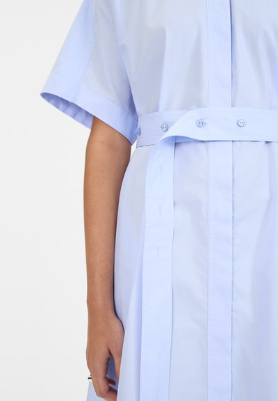 Abito button-up blu chiaro con maniche corte, cintura regolabile in vita e tessuto di cotone morbido. Presenta due tasche frontali e una vestibilità comoda.