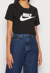 Camiseta de algodón negra con un logo de Nike blanco en el pecho, combinada con unos vaqueros de mezclilla azul de cintura alta con un corte clásico y bolsillos.