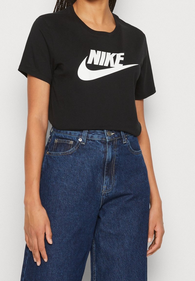 Camiseta de algodón negra con un logo de Nike blanco en el pecho, combinada con unos vaqueros de mezclilla azul de cintura alta con un corte clásico y bolsillos.