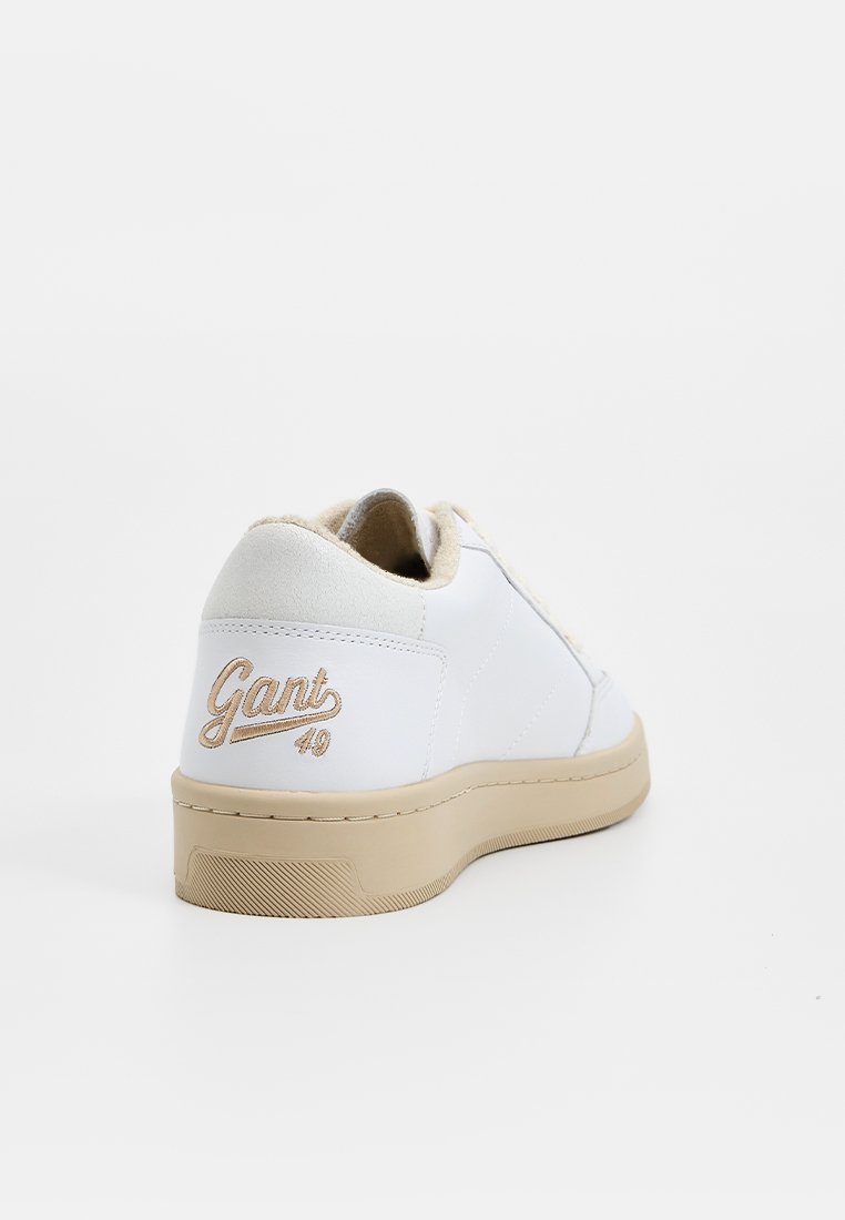 Zapatilla blanca con suela beige, con un upper de cuero liso y suaves acentos de ante. Logo "Gant" bordado en dorado en el talón.