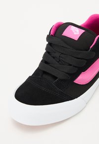 Mustad sneaker roosa aktsentidega, millel on samet- ja kangasmaterjalid, nööbitav sulgemine, ümar varvas ja valge kummist tall.