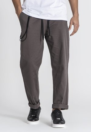 Gray lightweight trousers with a relaxed fit, featuring an elastic waistband and drawstring. Paired with black sneakers and cuffed hems.