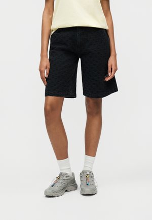 Osoba nosiaca čierne textúrované šortky po kolená, biele ponožky, sivé tenisky s farebnými jazdcami na šnúrkach a svetložltý top.