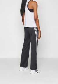 Svarta sportiga byxor med vita sidostripes, ihop med en vit tanktop och svarta underkläder. Modellen bär vita sportskor.