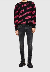 Suéter negro con texto gráfico rosa, combinado con jeans negros desgastados y zapatillas negras con cordones con acentos y acabado texturizado.