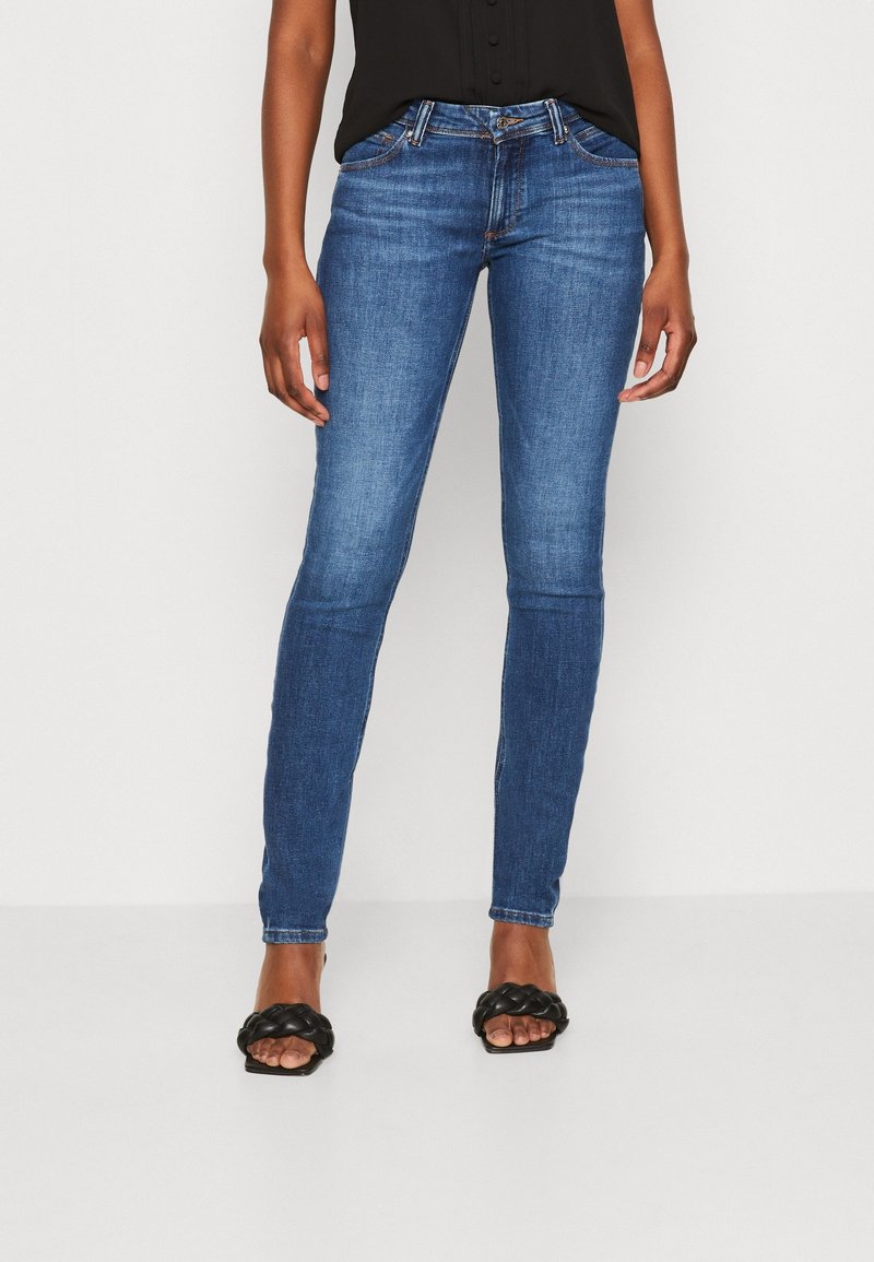 Slim džíny modré barvy vyrobené z džínoviny, s klasickým pětikomorovým designem a středním pasem. Doplněno černými hladkými sandály na ploché podrážce.