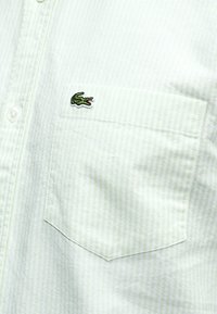 Chemise blanche à boutons avec de fines rayures vertes, dotée d'une poche poitrine et d'un petit logo crocodile vert brodé.