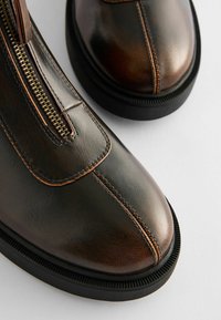 Brown leather ankle boots with a zip closure, contrasting stitching, and a textured black rubber sole. Smooth, shiny finish.