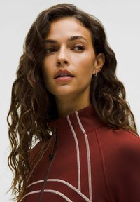 Giacca zip-up color marsala con dettagli in cucitura bianca; presenta un colletto alto e un design aderente. Indossata con capelli mossi, senza accessori visibili.