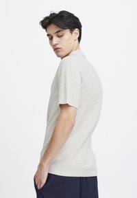 Beige kortermet polo skjorte med teksturert stoff, flat krage og ribbet kant. Plagget har et subtilt mønster og en avslappet passform.