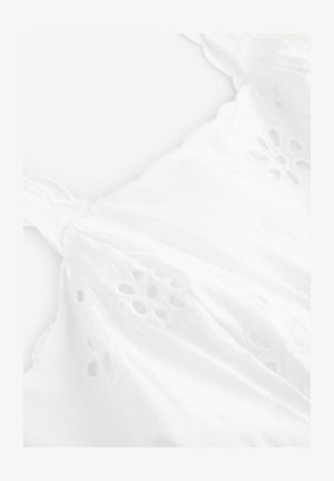 Biała odzież z delikatnym haftem, przedstawiającym kwiatowe wzory z wycięciami, miękka w dotyku, z falbaniastymi brzegami. Regulowane ramiączka.