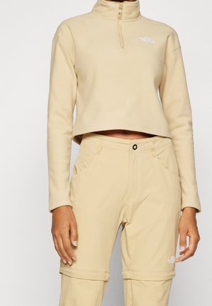 Beige korte fleece pullover met halve ritssluiting en bijpassende beige om te vormen broek met knoopsluiting en The North Face logo op beide.