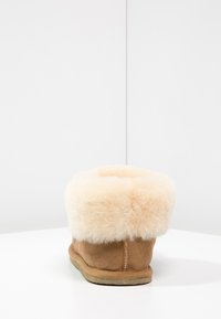 Stivale in suede beige con un morbido risvolto in shearling crema, forma tonda, suola piatta e dettagli minimi.