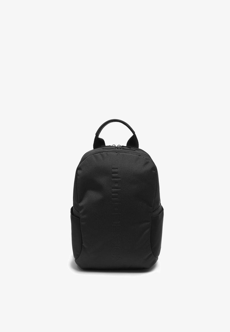 Sac à dos compact noir avec une poignée supérieure, une fermeture éclair avant et des poches latérales, posé debout sur un fond blanc.