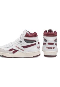 Biele vysoké tenisky Reebok v marónovej farbe, s hladkým koženým zvrškom, polstrovaným golierom a štruktúrovanou gumovou podrážkou s akcentmi značky.