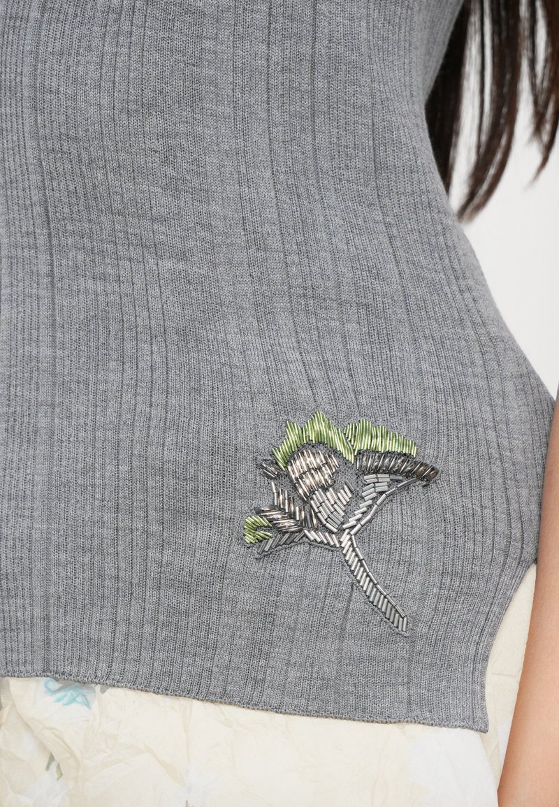 Grau gestreifter Strickoberteil mit einem floralen Stickdesign in grünen und silbernen Fäden, das sich auf der unteren linken Seite befindet.