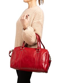 Borsa in pelle rossa con texture lucida e doppi manici. Caratterizzata da chiusura con zipper, tasca laterale e dettagli metallici.