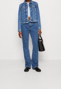 Denim jacket and high-waisted jeans in blue, paired with a black handbag. Boots with a chunky sole are worn, adding structure to the outfit.