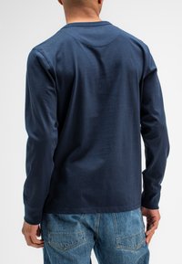 Marineblaues Langarm-T-Shirt mit klassischem Rundhalsausschnitt, aus weichem Baumwollstoff und entspannter Passform, kombiniert mit hellen Jeans.