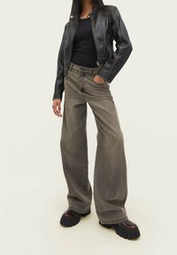 Black leather jacket with white stitching, fitted top, and wide-leg gray jeans with a high waist. Chunky black platform shoes.