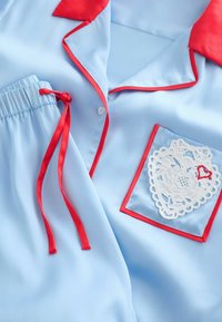 Világoskék szatén pizsama piros szegéllyel, piros gallérral, piros derékszalagokkal és csipke szívfolttal a mellzsebén.