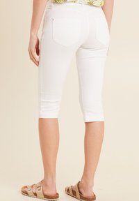 Witte capri jeans met een getailleerd ontwerp, voorzien van achterzakken en gestikte details langs de zijkanten, gecombineerd met een paar bruine sandalen.