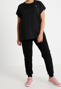 Svart t-shirt med korta ärmar och rund halsringning, i kombination med svarta avsmalnande byxor och rosa träningsskor. Lättviktigt tyg, avslappnad passform.