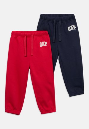 Kaksi paria lasten collegehousuja, yksi punainen ja yksi tummansininen, kumpikin joustavalla vyötäröllä ja lahkeensuilla, ja valkoinen "GAP"-logo vasemmassa lonkassa.