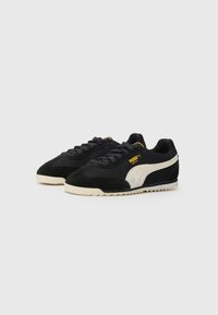 Zapatillas de ante negro con paneles de malla, logo blanco de Puma y acentos en amarillo. Presentan una suela de goma texturizada y un diseño de cordones.